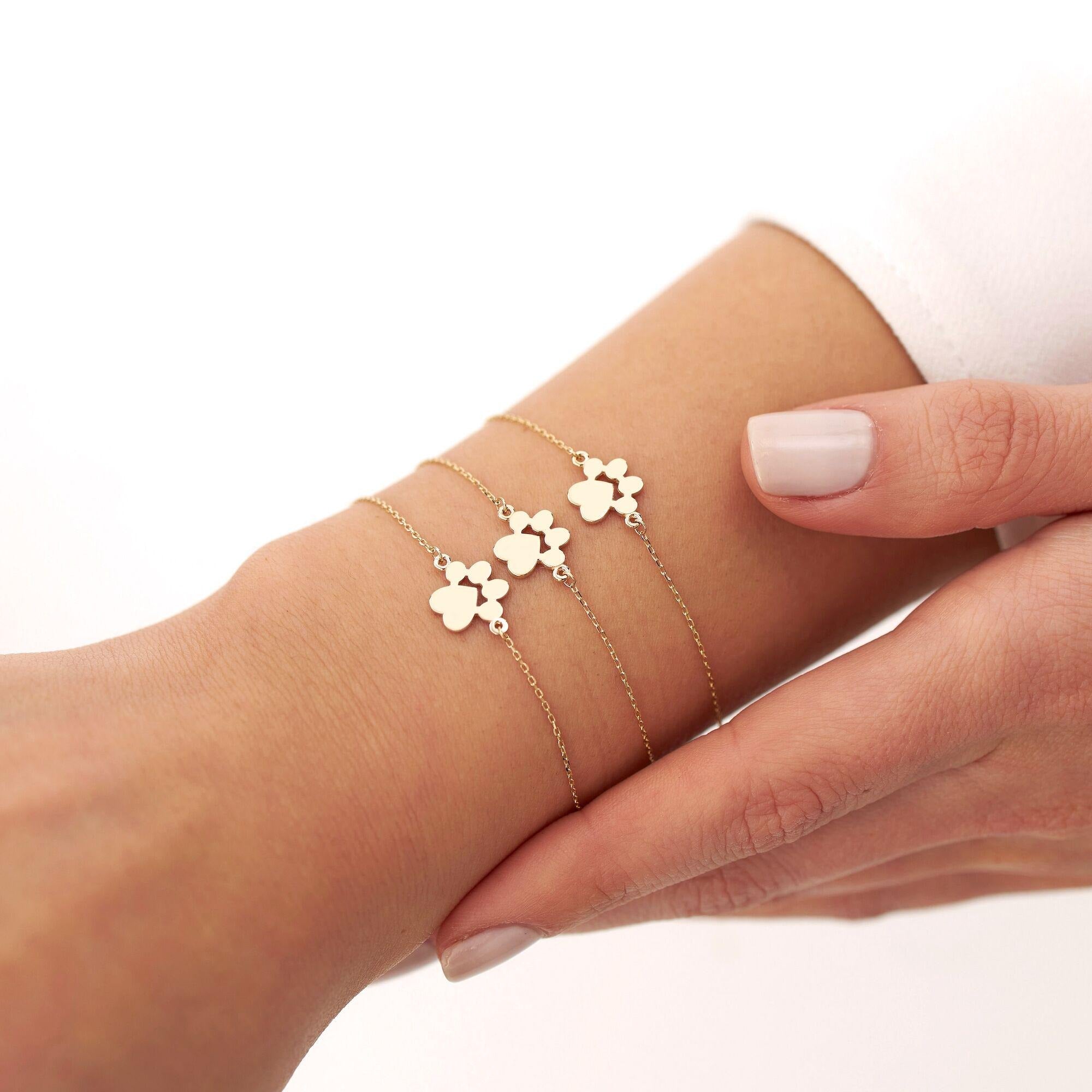 Multiple Luxurious 14K Gold Paw Bracelets stacked elegantly on a wrist, celebrating pet love and style.